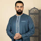 Portrait of Malik Idris, a man with a confident expression, wearing a MOONQADIR garment against a cream background.